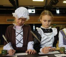 two girls dressed in tudor day costumes writing with quills and ink