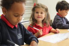 three children sitting at a table writing on paper