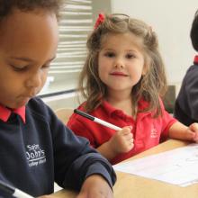 three children sitting at a table writing on paper