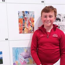 pupil standing next to his artwork at an exhibition 